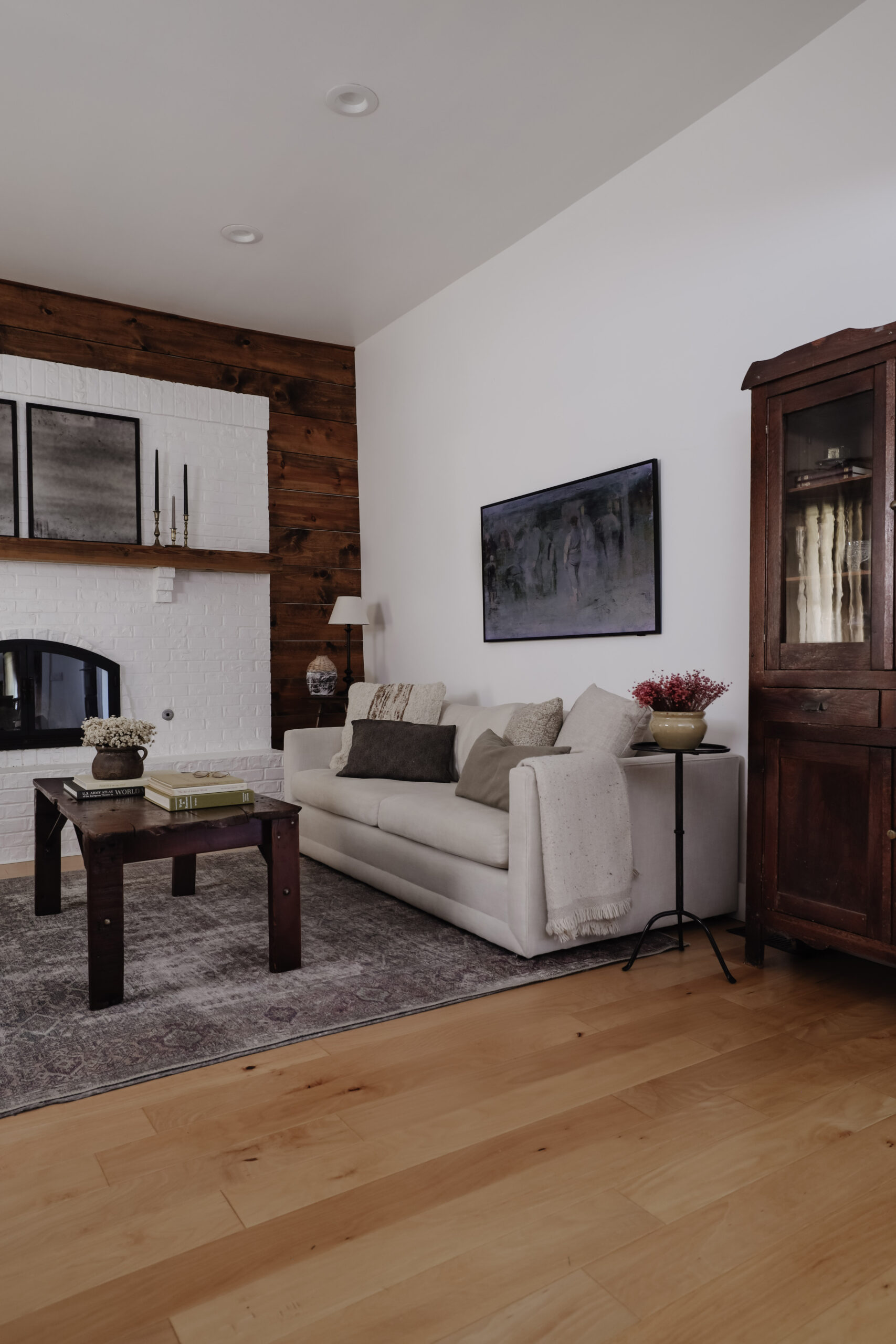 Living room with wood shiplap walls and brick fireplace. Casual sofa and antique hutch.
