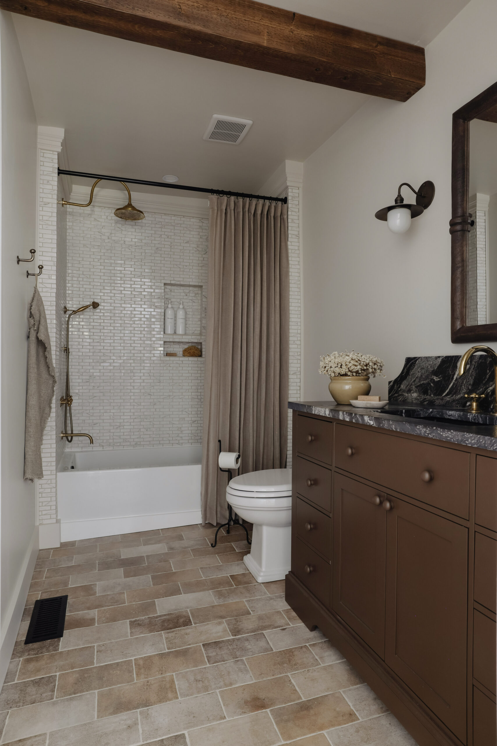 Dramatic bathroom before and after. Brown vanity with black and white veined granite countertop. Marble mosaic shower tile. Unlacquered brass shower head and faucet. Nadine Stay