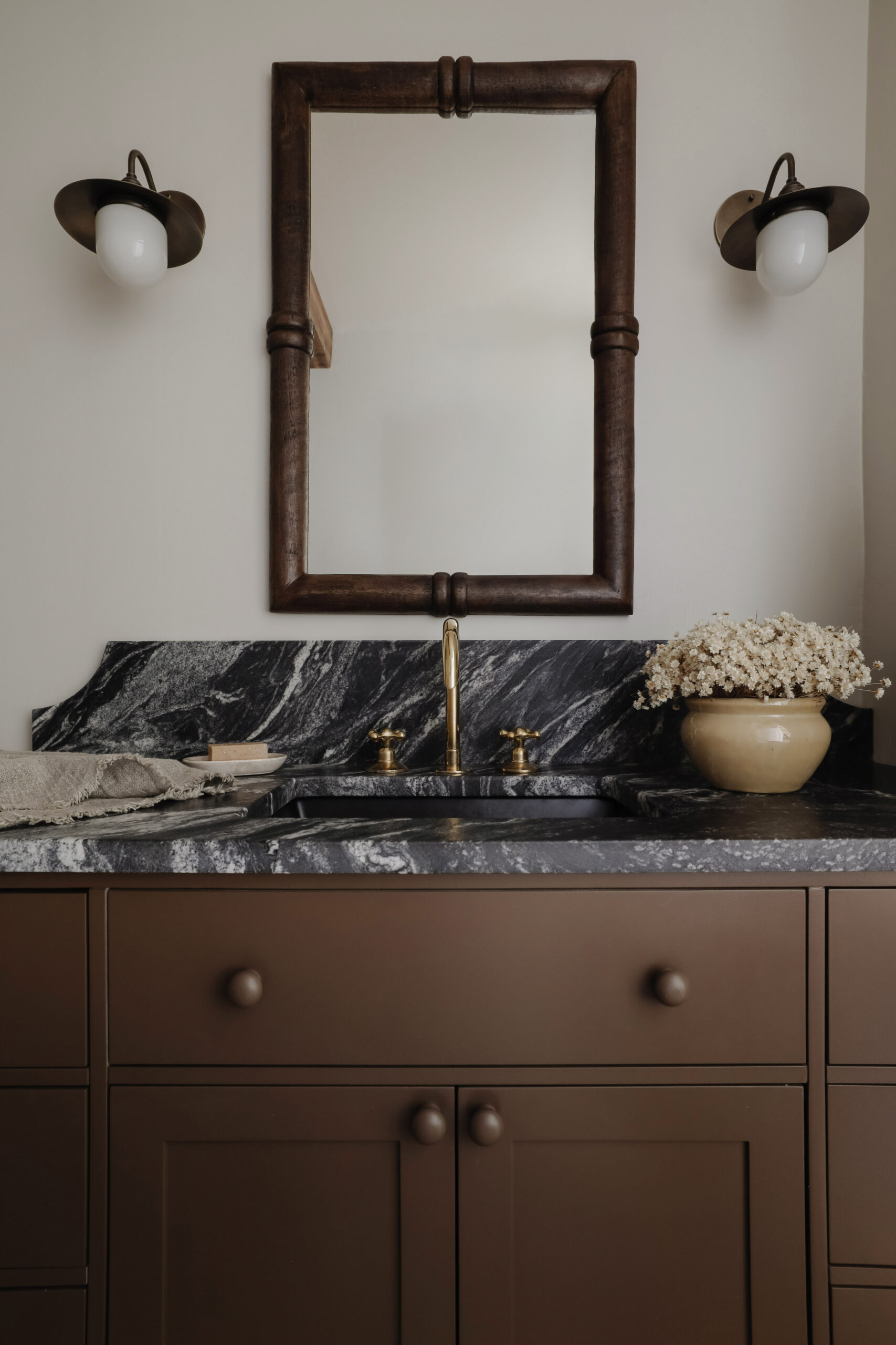 Brown vanity and bathroom wood mirror with black and white veined granite countertop. Nadine Stay