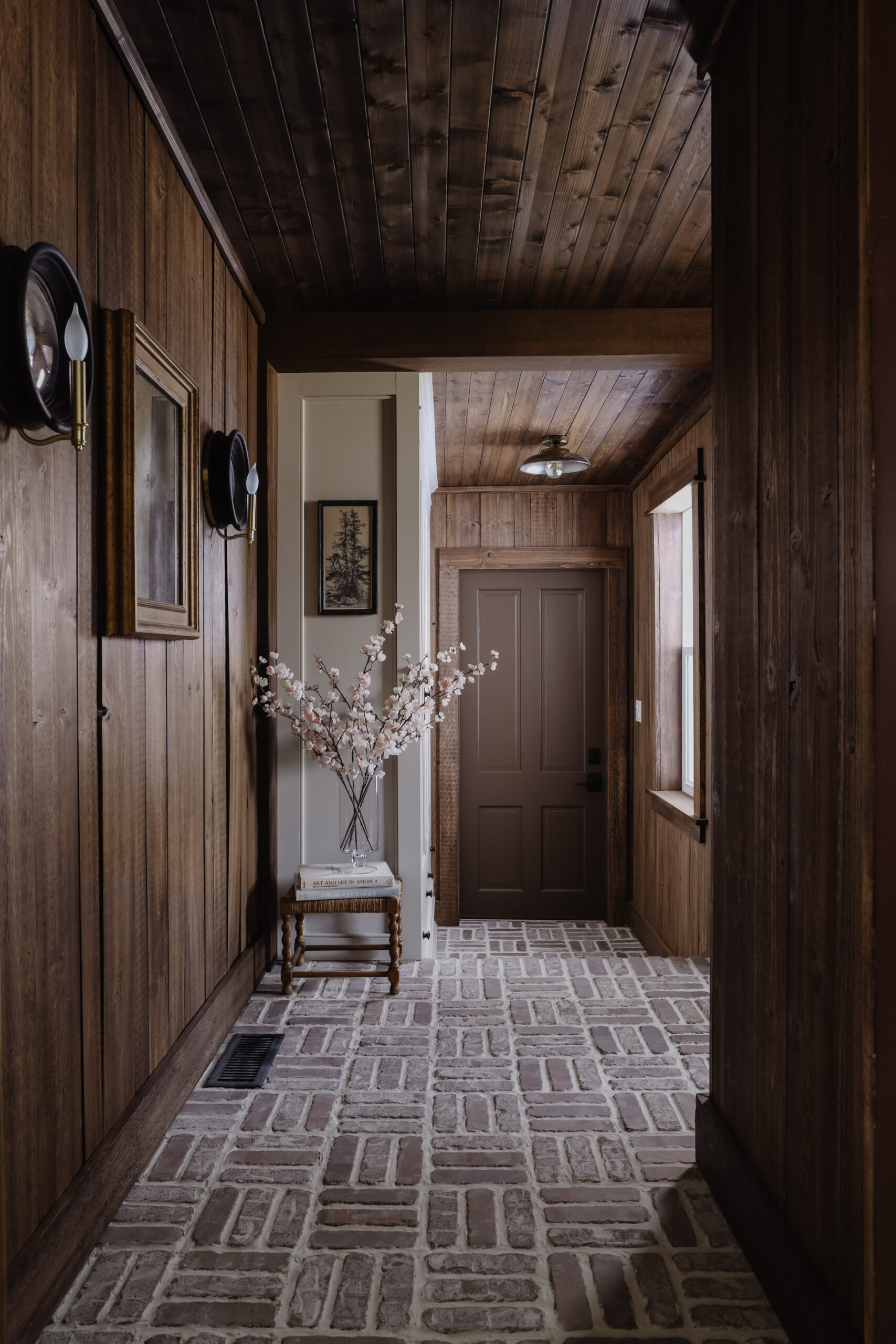 Dark wood vertical paneling in a mudroom with sconces and flush mount light. | Nadine Stay