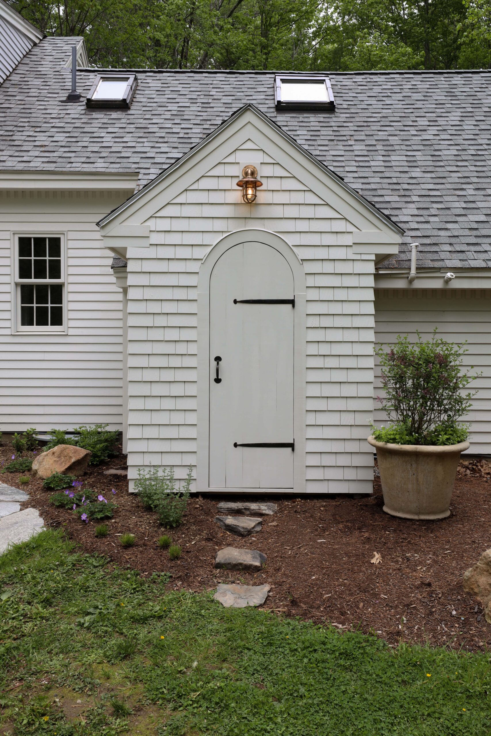 White garden shed with arched plank door and antique ship light sconce. Nadine Stay