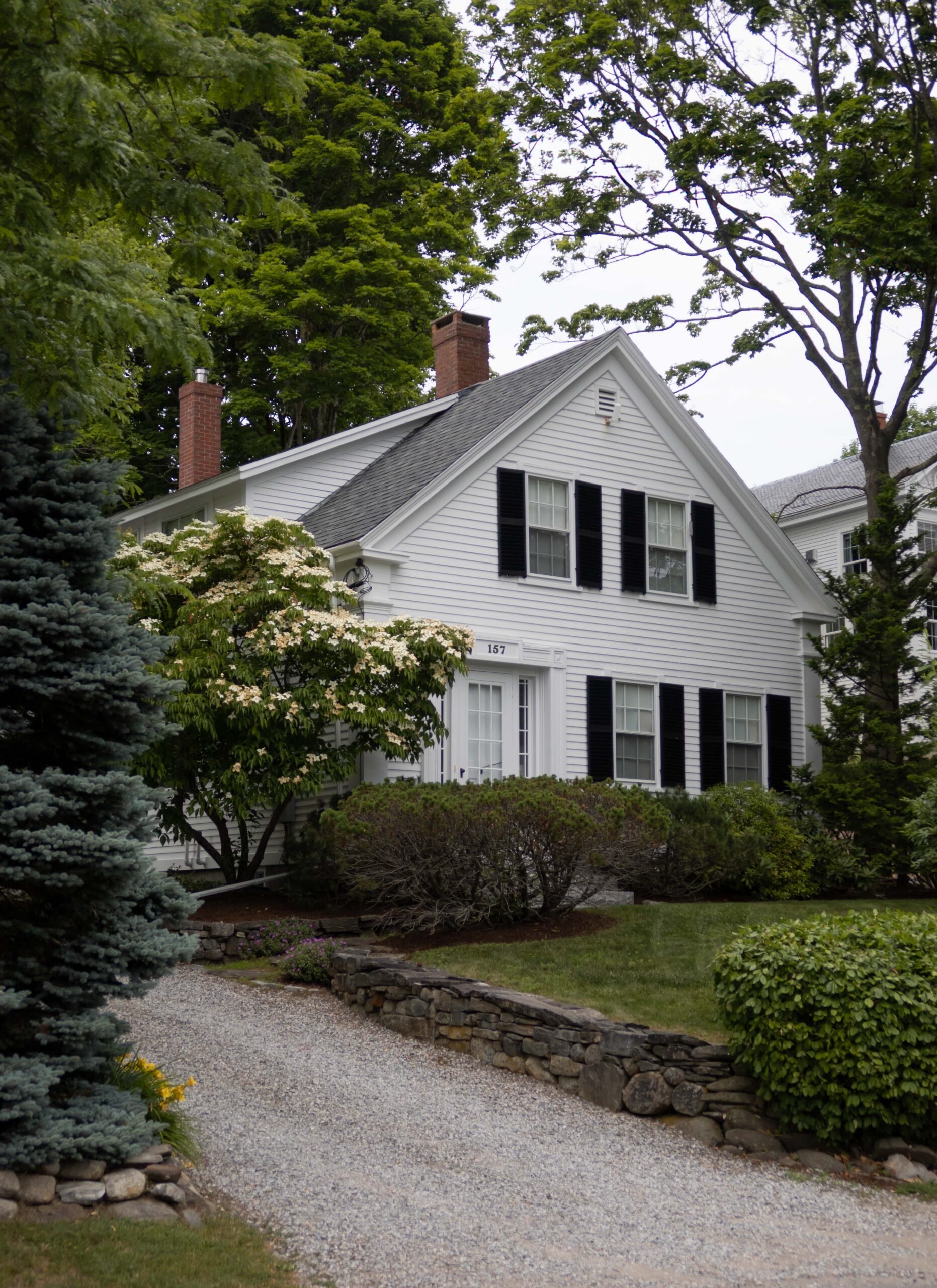 Early New England home with black wood functional shutters and white wood siding - Nadine Stay
