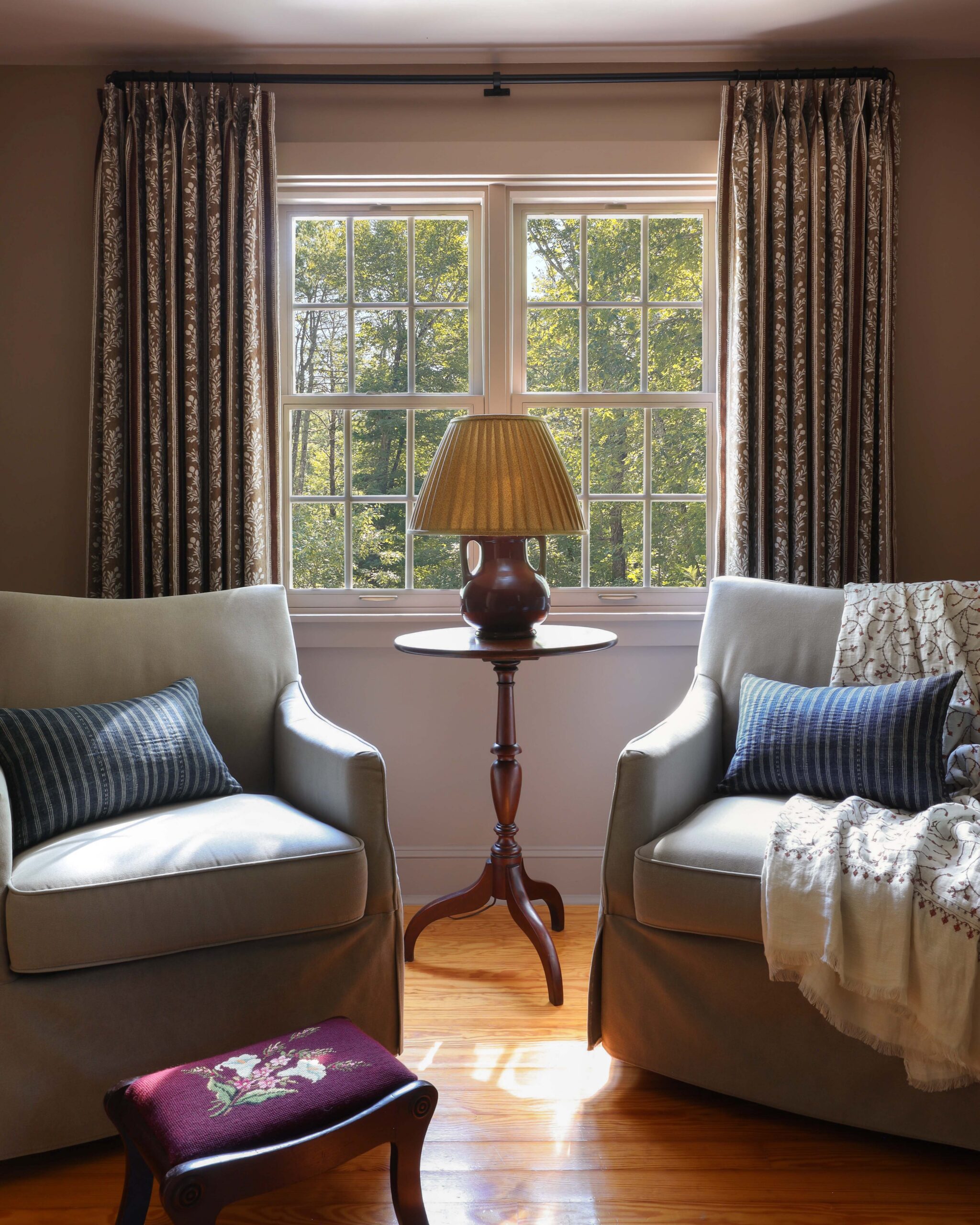 Bedroom with burgundy floral pinch pleated curtains and green slipcover chairs. Yellow pleated lampshade. Nadine Stay