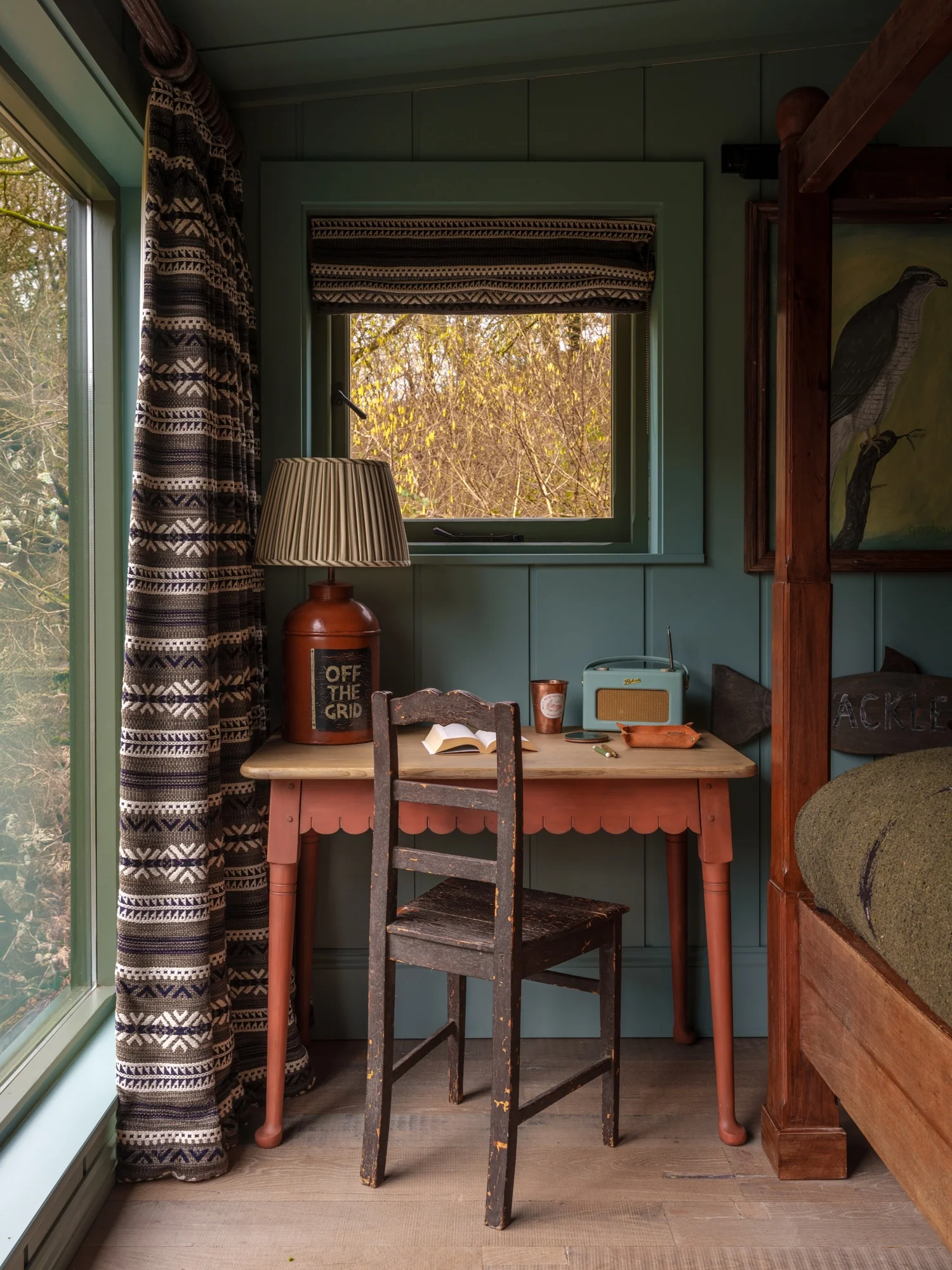 Cabin bedroom with blue green wood planks on the walls and ceiling. A charming red desk sits in the corner. HÁM Interiors